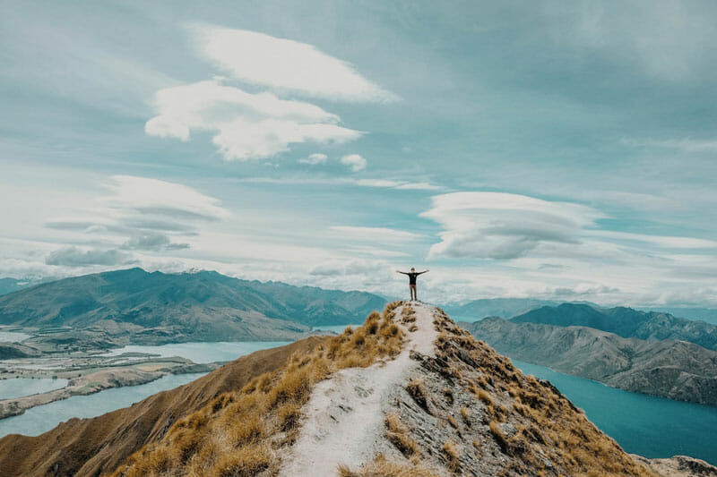man on top of a mountain peak looking over lake