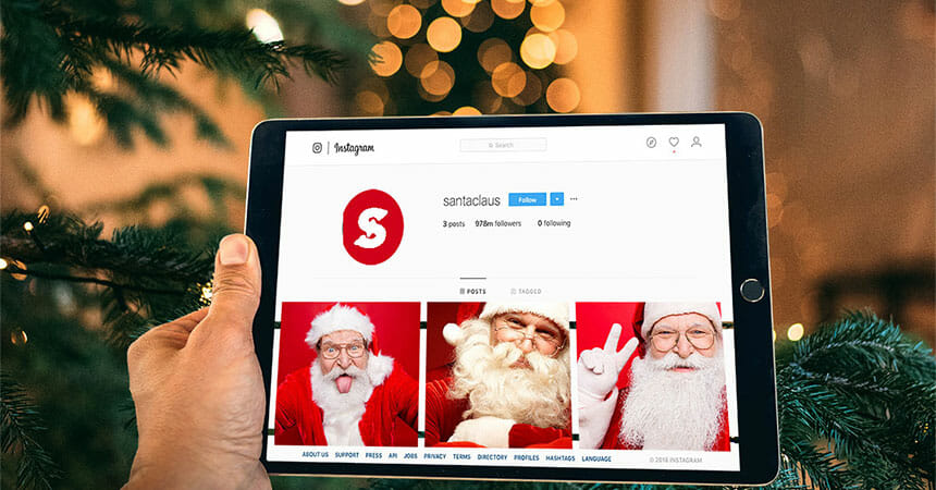 hand holding ipad displaying santa claus's instagram page in front of a christmas tree
