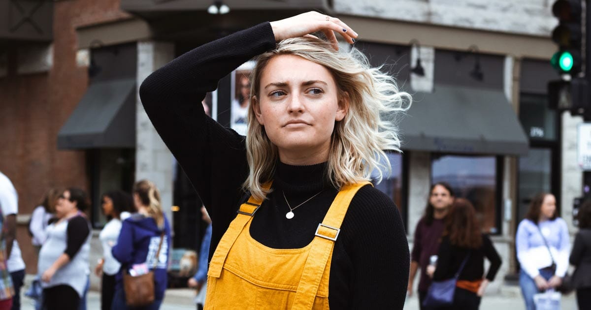 blonde woman in black turtleneck and yellow overalls thinking while crossing street