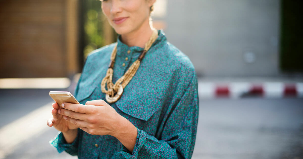 smiling woman in blue blouse and statement necklace holding gold iphone